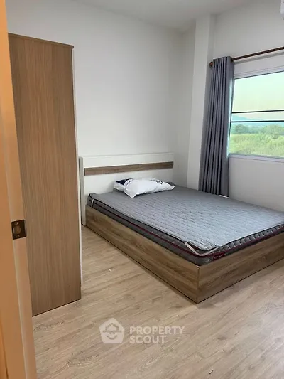 Cozy bedroom with wooden flooring and large window offering natural light
