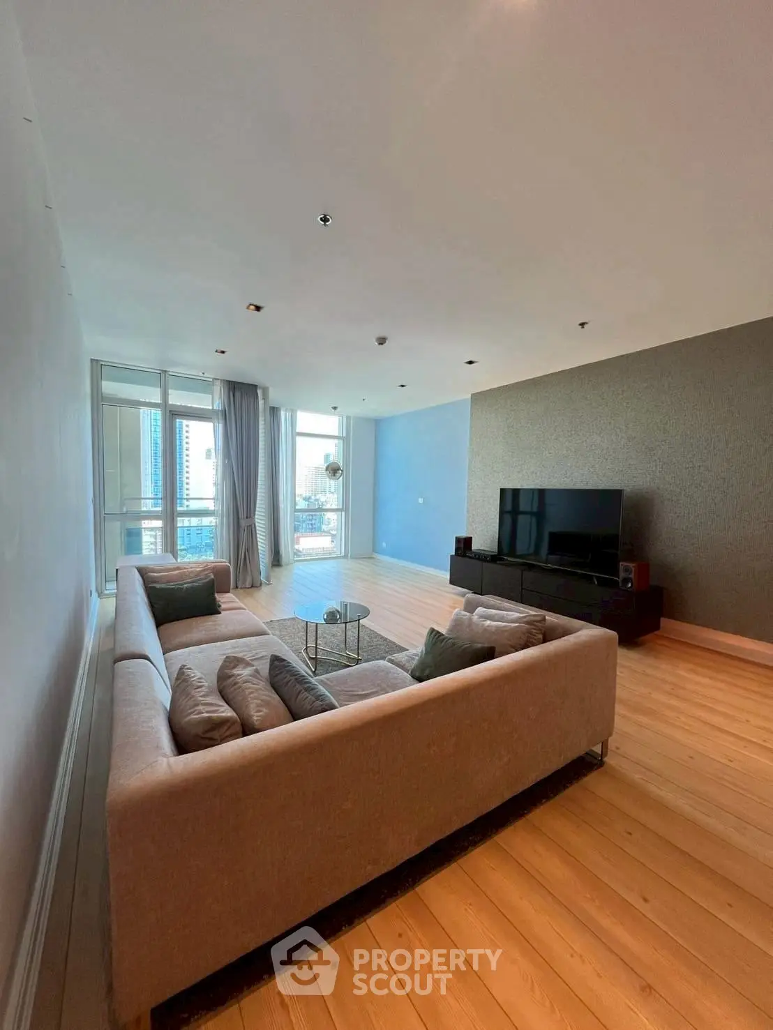 Spacious modern living room with large sofa and city view balcony.