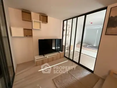 Modern living room with sliding glass doors leading to a cozy bedroom, featuring stylish shelving and a flat-screen TV.
