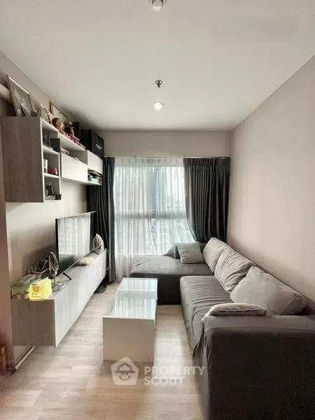 Modern living room with cozy gray sofa and entertainment center, featuring large window with curtains.