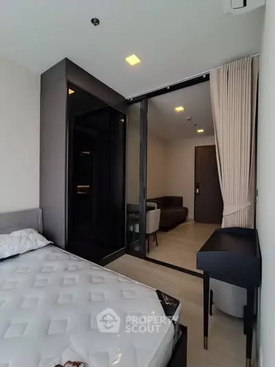 Modern bedroom with sliding glass doors leading to a cozy living area, featuring sleek furniture and neutral tones.