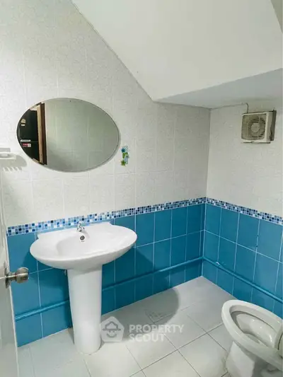 Compact bathroom with blue and white tiles, featuring a pedestal sink and wall mirror.