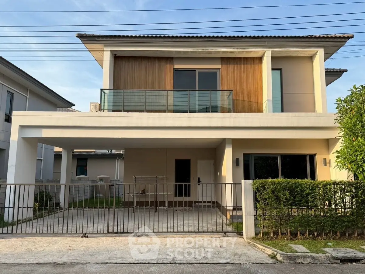 Modern two-story house with balcony and gated driveway in suburban neighborhood.