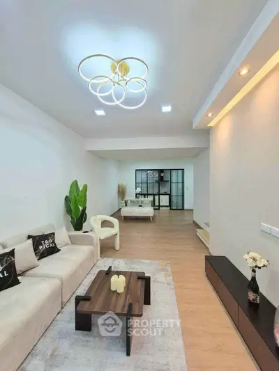 Modern living room with stylish lighting and open layout leading to a bedroom, featuring elegant decor and wooden flooring.