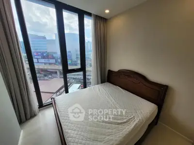 Cozy bedroom with large windows offering city views, featuring a classic wooden bed frame and neutral decor.