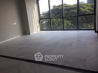 Spacious room with large windows and marble flooring, offering a serene view of lush greenery.