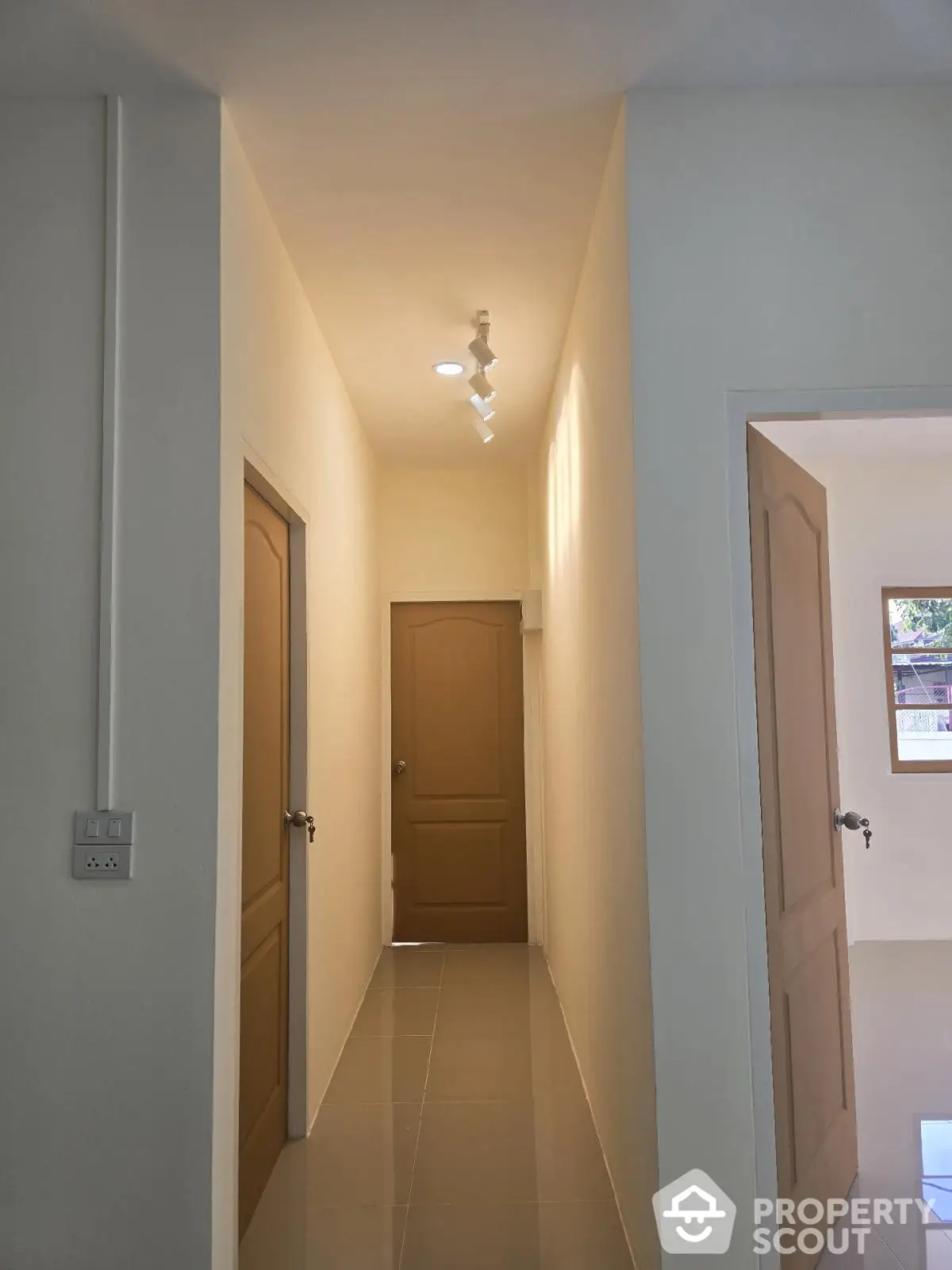 Bright hallway with modern lighting and neutral tones, leading to multiple rooms with sleek doors.