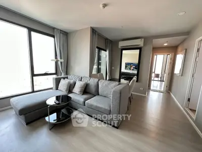 Modern living room with gray sofa, sleek decor, and natural light from large windows.