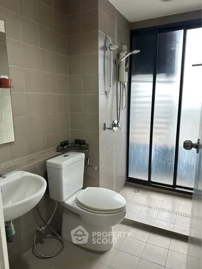 Modern bathroom with shower and frosted glass door, featuring sleek fixtures and neutral tiles.