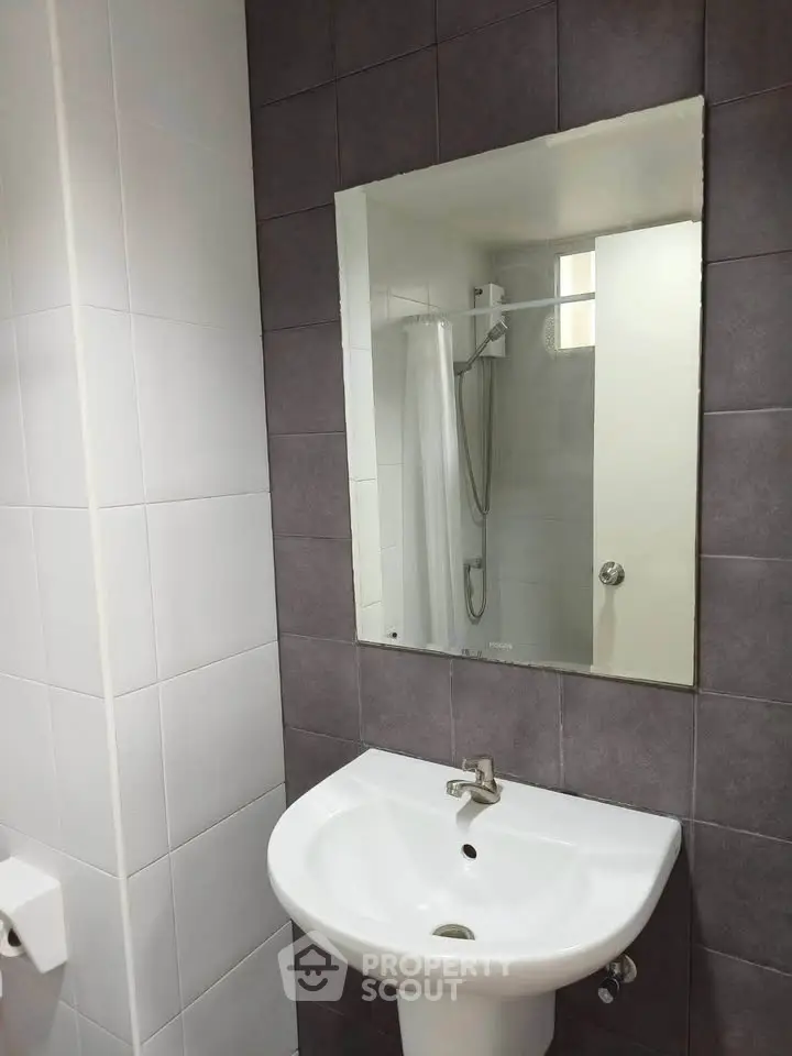 Modern bathroom with sleek sink and mirror, featuring a shower area with elegant tile design.
