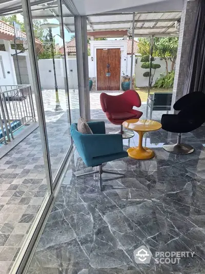 Stylish modern living area with vibrant chairs and marble flooring overlooking a spacious patio.