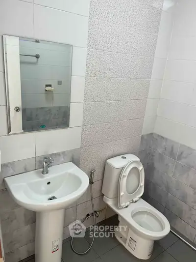 Modern bathroom with sleek sink and toilet in a tiled setting.