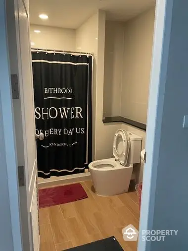 Modern bathroom with stylish black shower curtain, pristine white toilet, and elegant red bath mat, offering a cozy and inviting atmosphere.