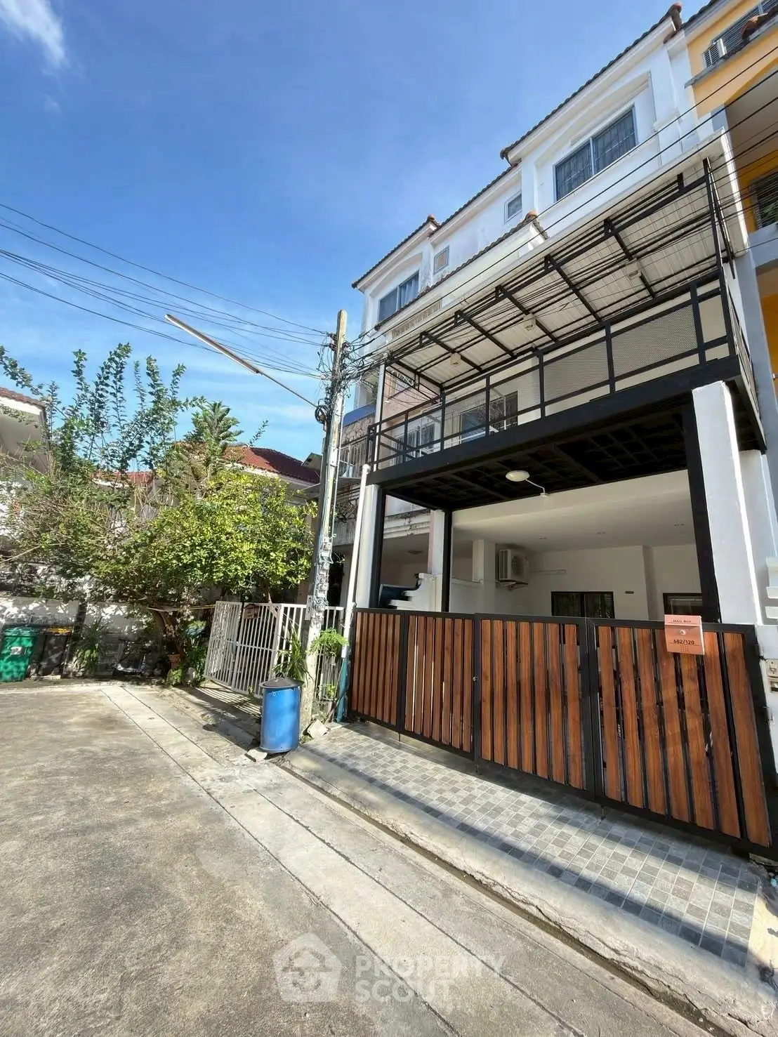 Modern three-story townhouse with gated entrance and balcony in sunny neighborhood.