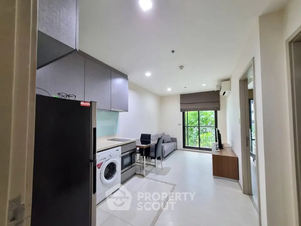 Modern apartment interior with kitchen and living area, featuring sleek appliances and large window view.
