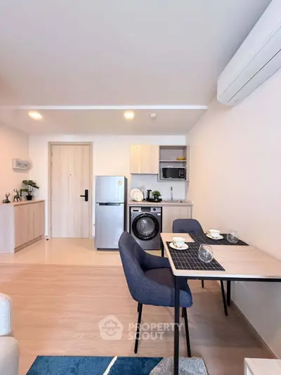 Modern open-plan living room with compact kitchen and dining area, featuring sleek appliances and stylish decor.