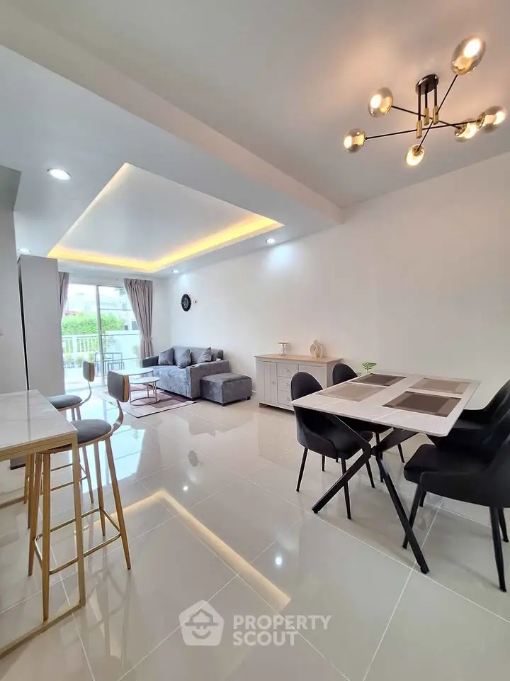 Spacious modern living room with open layout and elegant dining area, featuring stylish lighting and sleek furniture.
