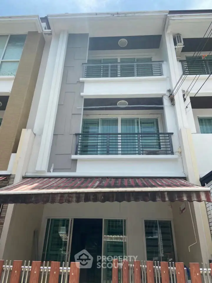 Modern three-story townhouse with balcony and awning, perfect for urban living.