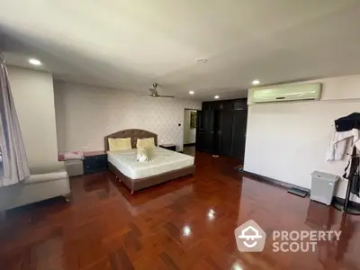 Spacious bedroom with polished hardwood floors, large bed, and modern air conditioning unit, offering a blend of comfort and luxury.