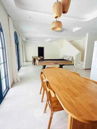 Spacious dining area with modern wooden table and chairs, featuring stylish lighting and a foosball table.