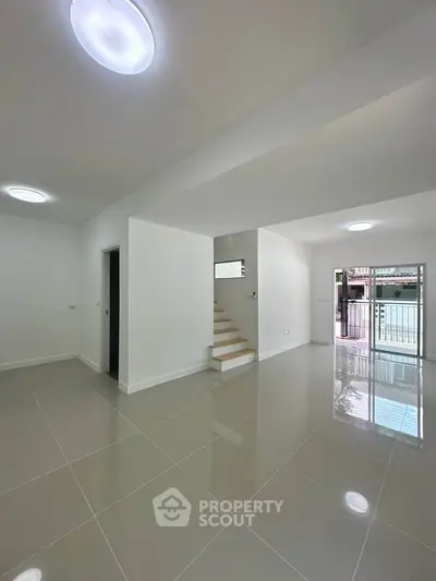 Spacious modern living area with glossy tiled floors and staircase, ideal for contemporary living.
