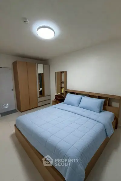 Cozy bedroom with modern wooden furniture and soft blue bedding, perfect for relaxation.