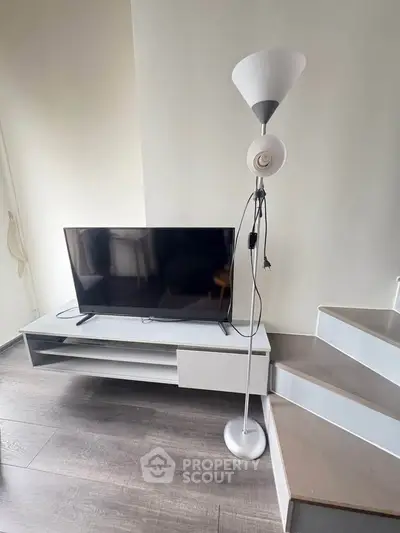 Modern living room with sleek TV stand and stylish floor lamp on wooden flooring.