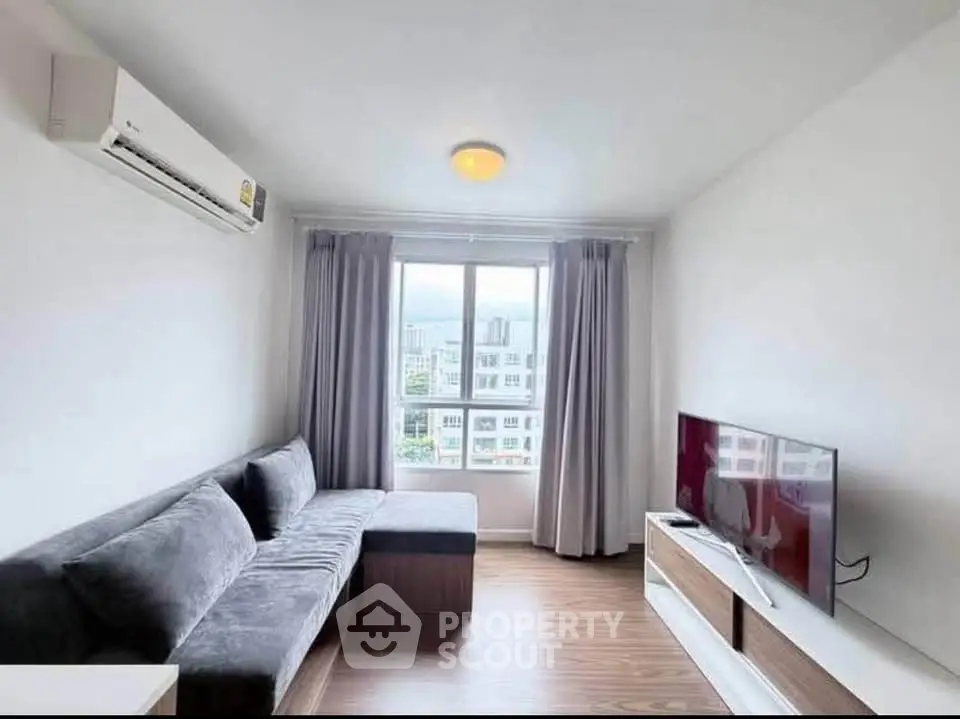 Modern living room with sleek furniture and large window offering city views.