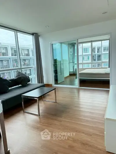 Modern apartment with open living room and bedroom, featuring large windows and sleek furnishings.