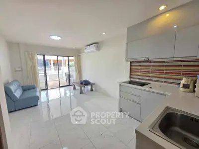 Modern living room with open kitchen and balcony access, featuring sleek design and natural light.