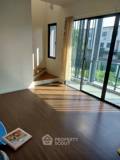 Bright living room with wooden floors and large windows overlooking greenery.