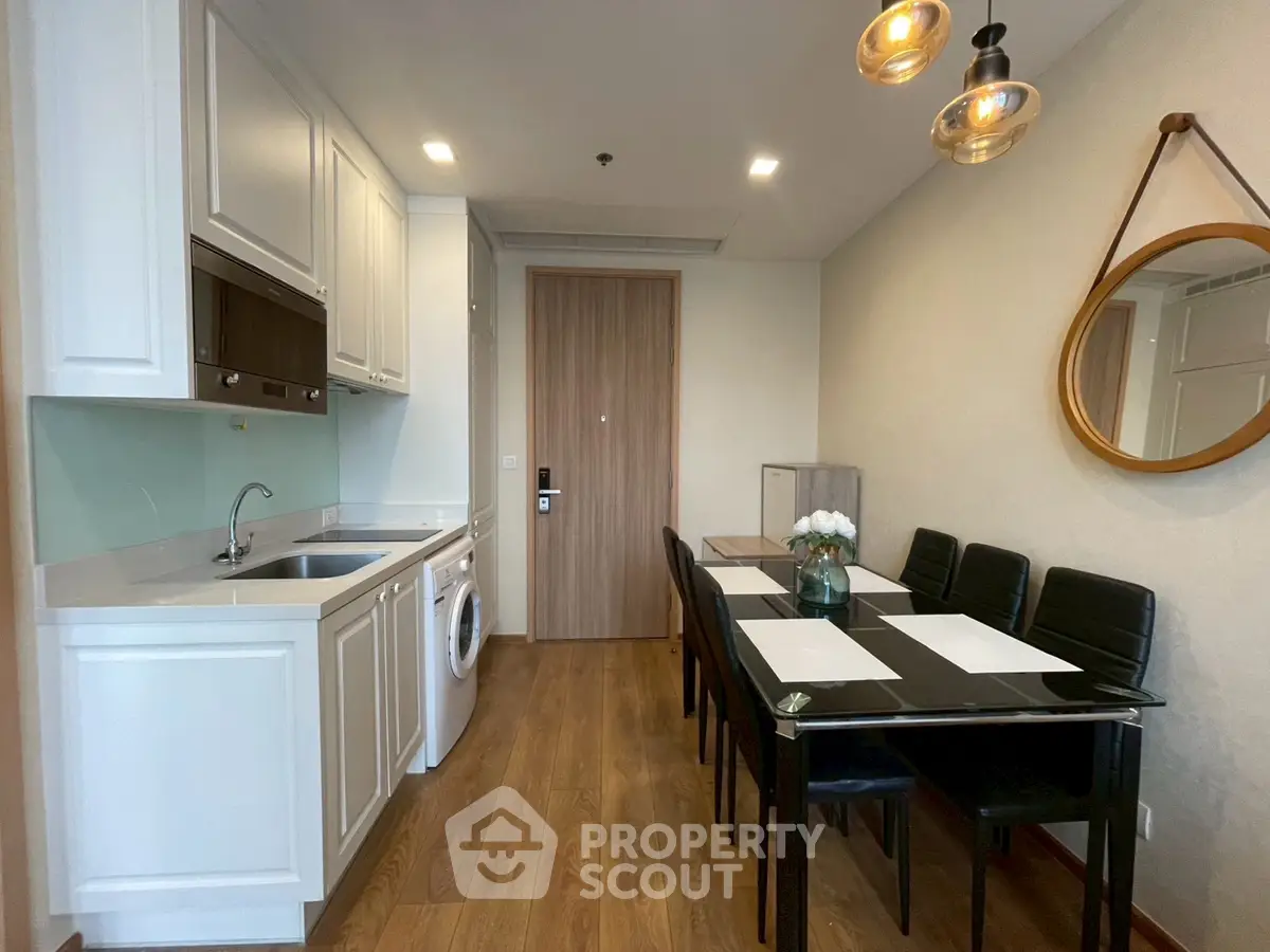 Modern kitchen with dining area, featuring sleek cabinetry and elegant lighting in a cozy apartment.