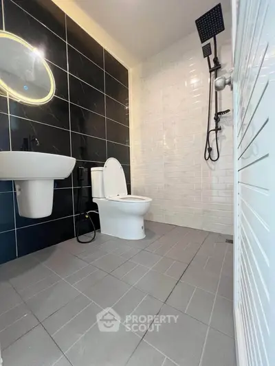 Modern bathroom with sleek black and white tiles, featuring a stylish shower and illuminated mirror.
