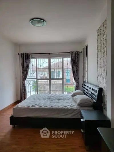 Spacious bedroom with large window and wooden flooring, offering a cozy and bright atmosphere.