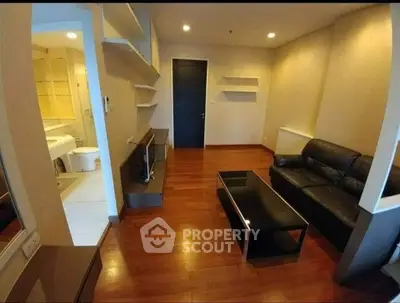 Modern living room with sleek black leather sofa and wooden flooring, adjacent to a stylish bathroom.