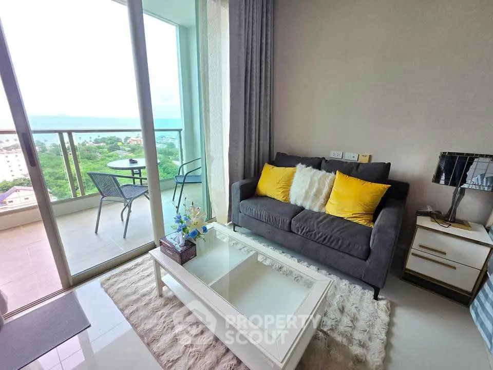 Modern living room with cozy sofa, vibrant cushions, and stunning balcony view of lush greenery and ocean.
