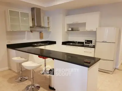 Modern kitchen with sleek black countertops and white cabinetry, featuring a breakfast bar and contemporary stools.