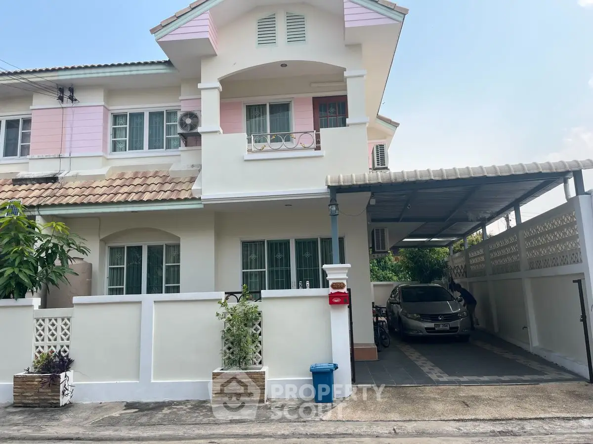 Charming two-story house with carport in a serene neighborhood, featuring pastel accents and lush greenery.