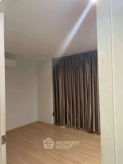 Spacious empty room with wooden flooring and large window with curtains, ideal for customization.