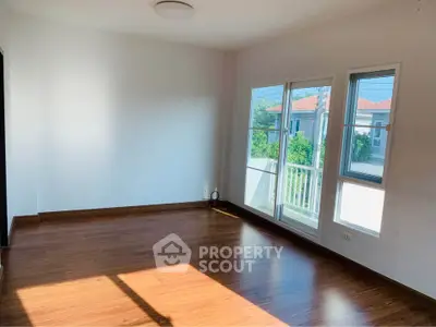 Spacious empty room with hardwood floors and large windows offering natural light.