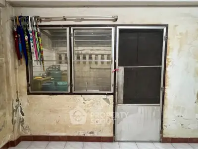 Rustic kitchen with metal door and window, colorful umbrellas, and visible gas cylinders.