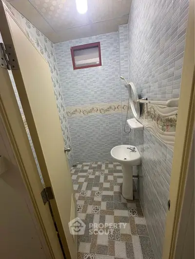 Compact bathroom with tiled walls and pedestal sink, featuring a small window for ventilation.