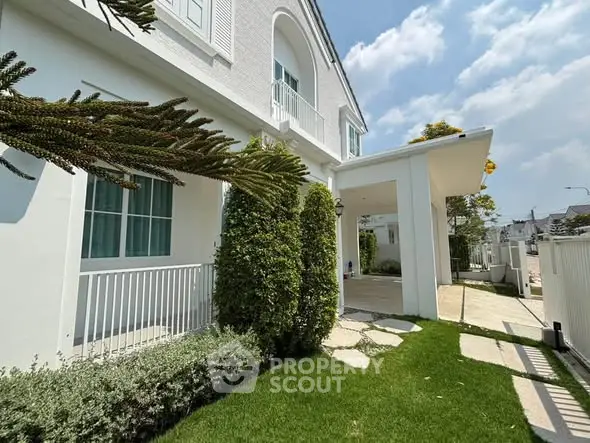 Charming white house exterior with lush green garden and inviting pathway under a clear blue sky.