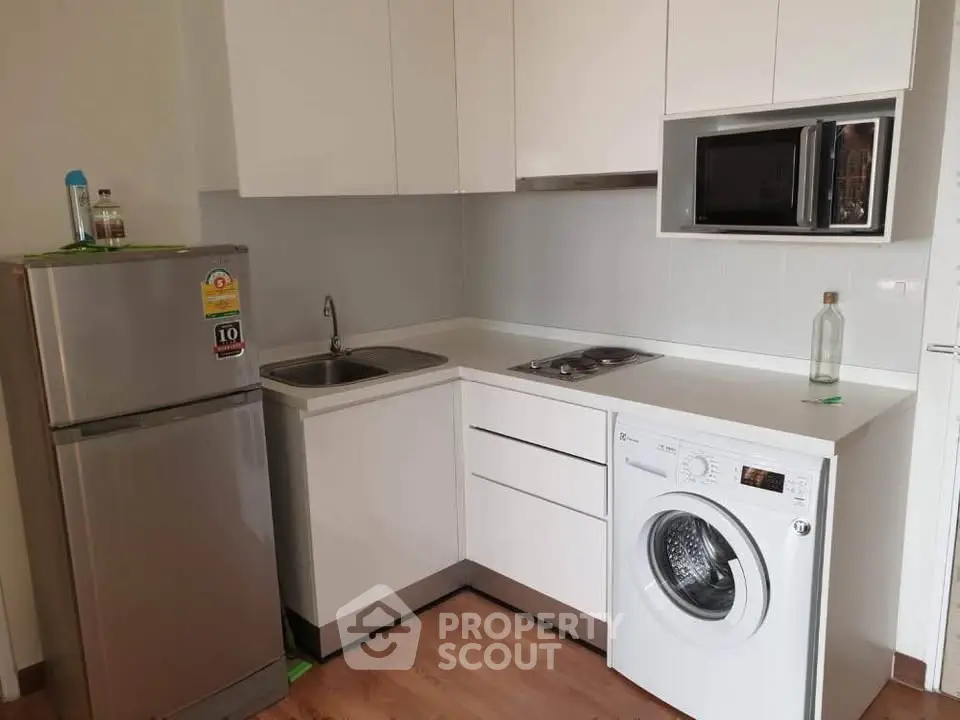 Modern compact kitchen with appliances including fridge, washing machine, and microwave in sleek white cabinetry.