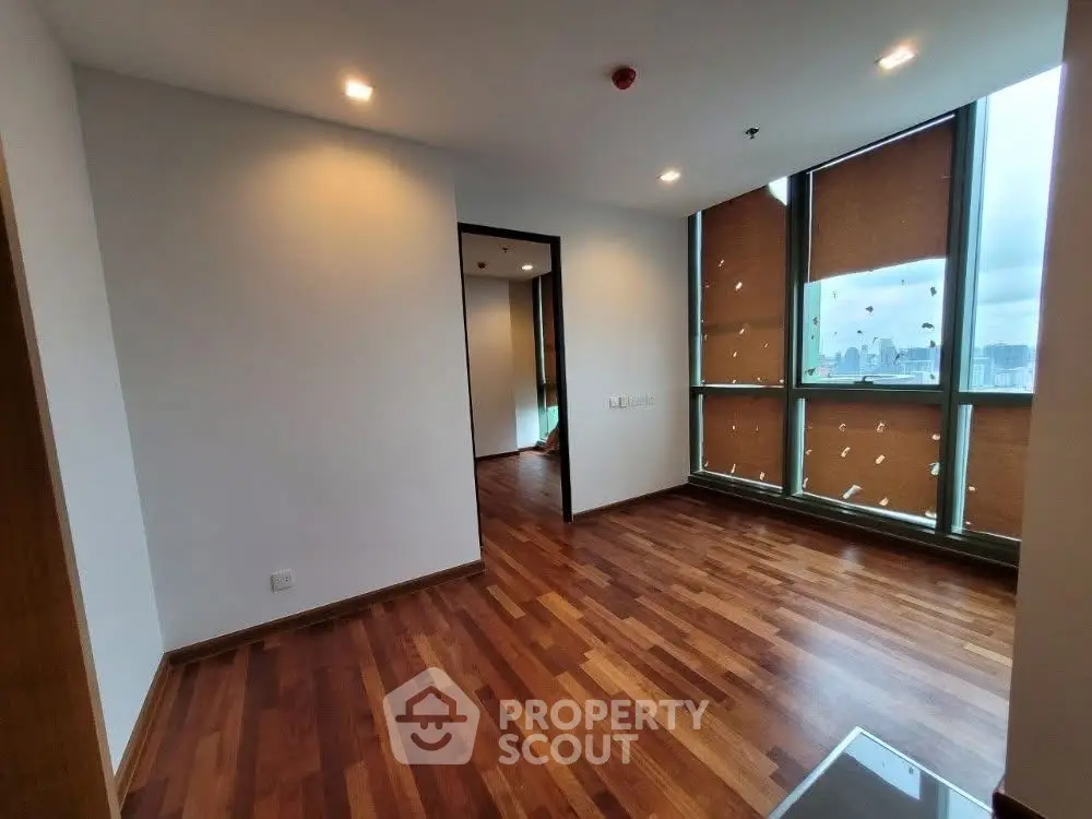 Spacious modern apartment with wooden flooring and large windows offering city views.