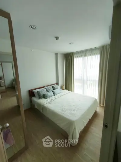 Bright and cozy bedroom with large window and wooden flooring, perfect for relaxation.