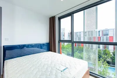 Modern bedroom with large window offering a stunning view of contemporary architecture and lush greenery.