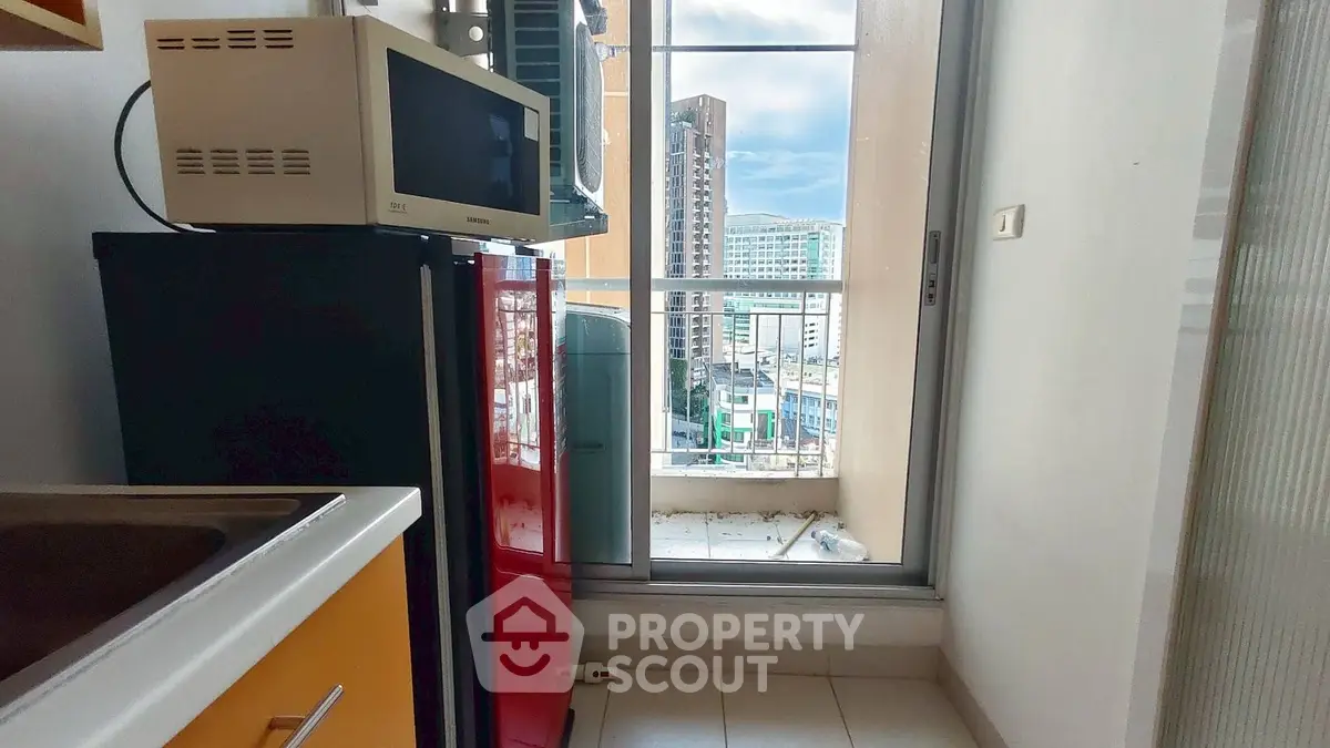 Compact kitchen with microwave and fridge, leading to a balcony with city view.