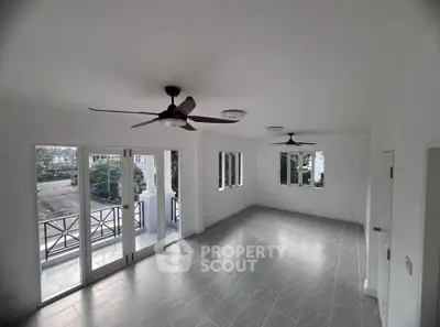 Spacious living room with ceiling fans and large windows opening to a balcony, offering ample natural light.