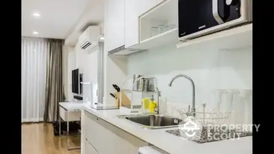 Sleek modern kitchen with white cabinetry and stainless steel sink, complemented by wooden flooring and a cozy living area in the background.